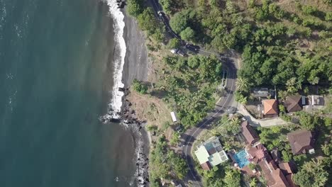 Toma-Aérea-De-La-Carretera-Cerca-De-La-Playa-Rocosa-Con-Agua-De-Mar-Salpicando-Las-Rocas-En-Bali