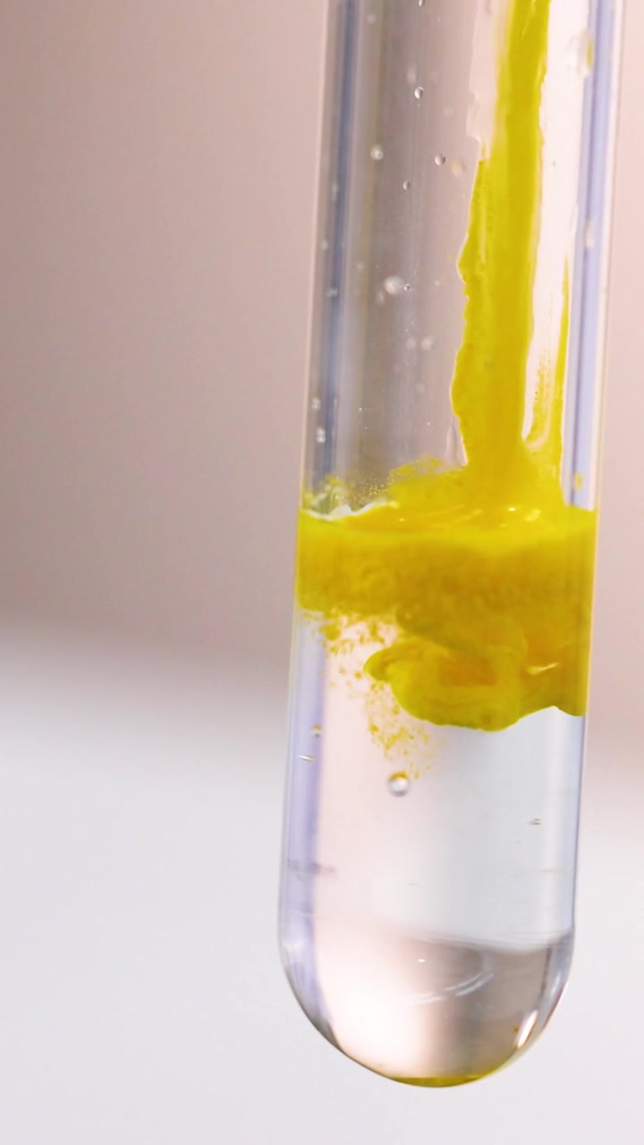 Una vivace reazione chimica gialla avviene all'interno di un liquido trasparente dentro una provetta verticale
