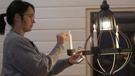 young dark-haired woman with glasses lights candles on chandelier