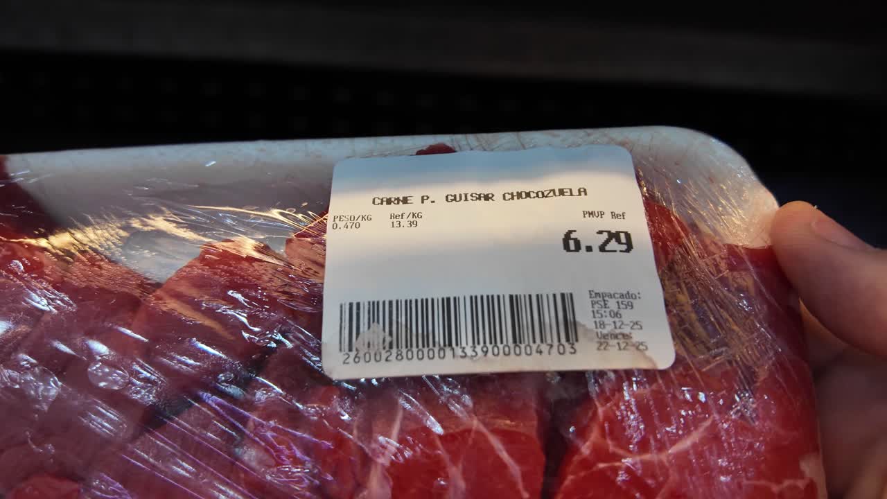 Close-up plastic-wrapped tray of carne de guisar raw beef displayed on refrigerated shelf in supermarket. Fresh red meat cuts food packaging, dolar pricing label, and everyday grocery shopping
