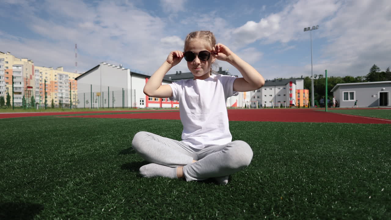 A little girl in sunglasses is running and smiling in the park. A stylish girl in a white T-shirt. A girl with braided hair