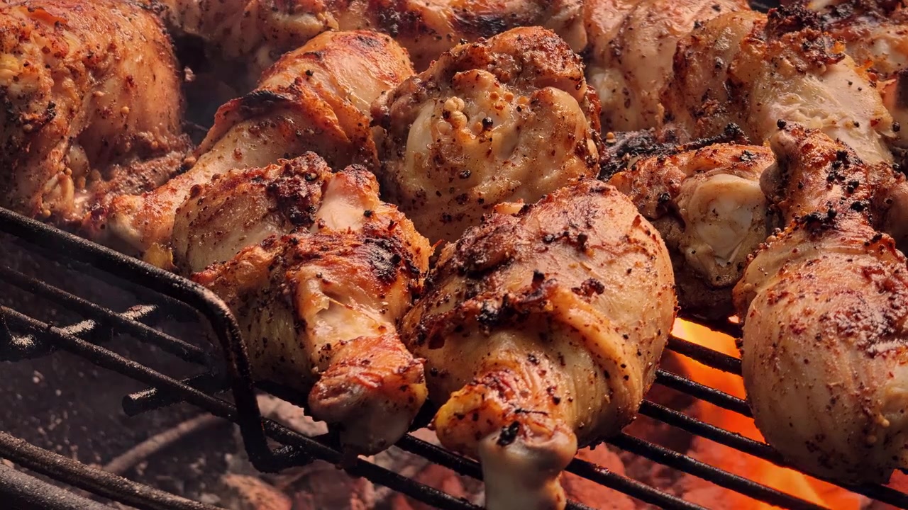 Muslos de pollo sazonados se sellan sobre brasas incandescentes mientras un humo ligero revela la piel dorada, los bordes carbonizados y la pátina oscura de una parrilla bien utilizada