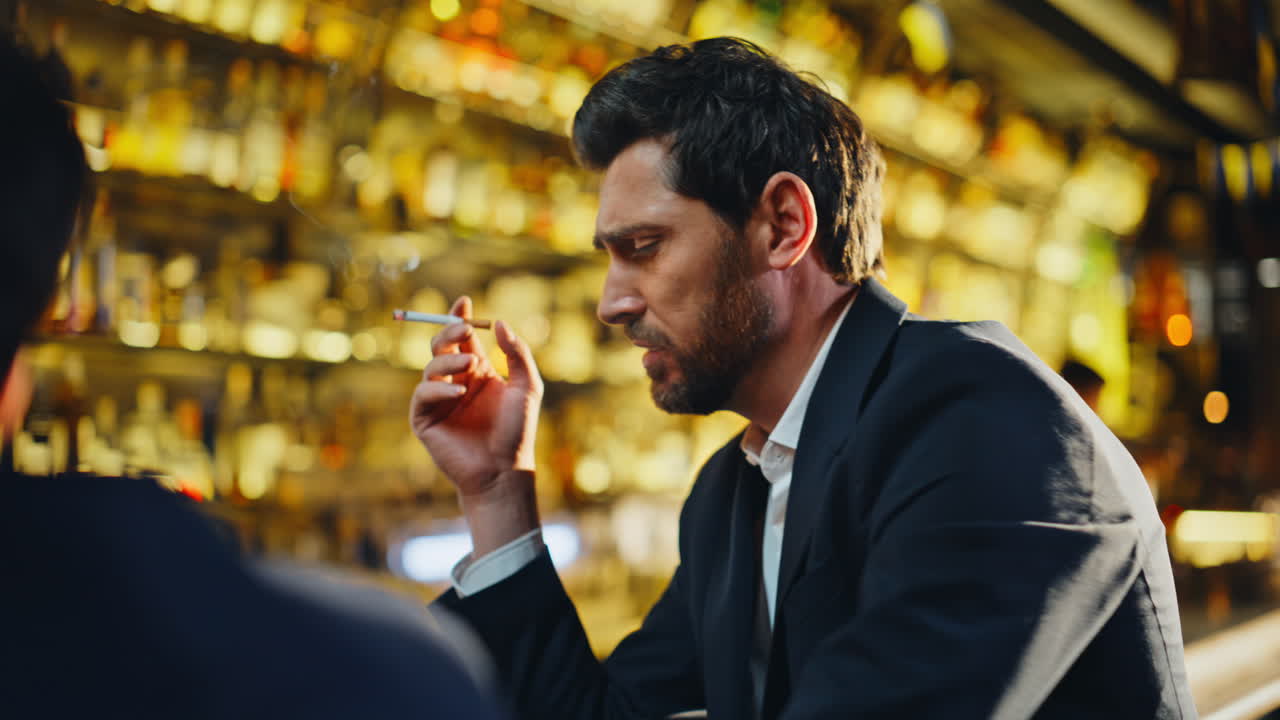 Uomo d'affari brillo che fuma seduto al bar, primo piano. Colleghi che si godono un drink