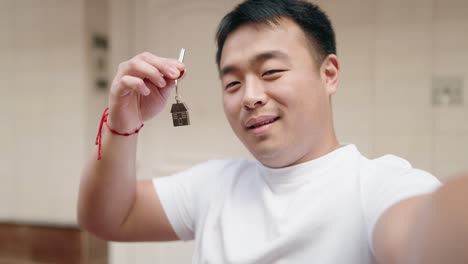 young chinese man holding key of new home having video call at street