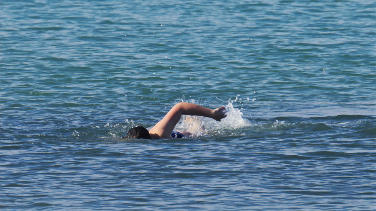 View of a man swimming in the blue Mediterranean Sea in daylight