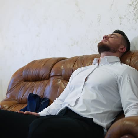 tired man resting after a long trip. handsome man in white shirt is sitting on a comfortable couch in a hotel room