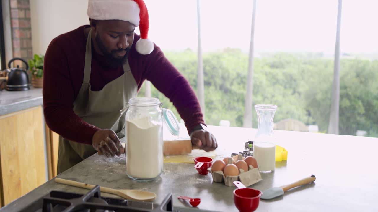African American man tapping flour, flattening with rolling pin for cookies on counter, copy space