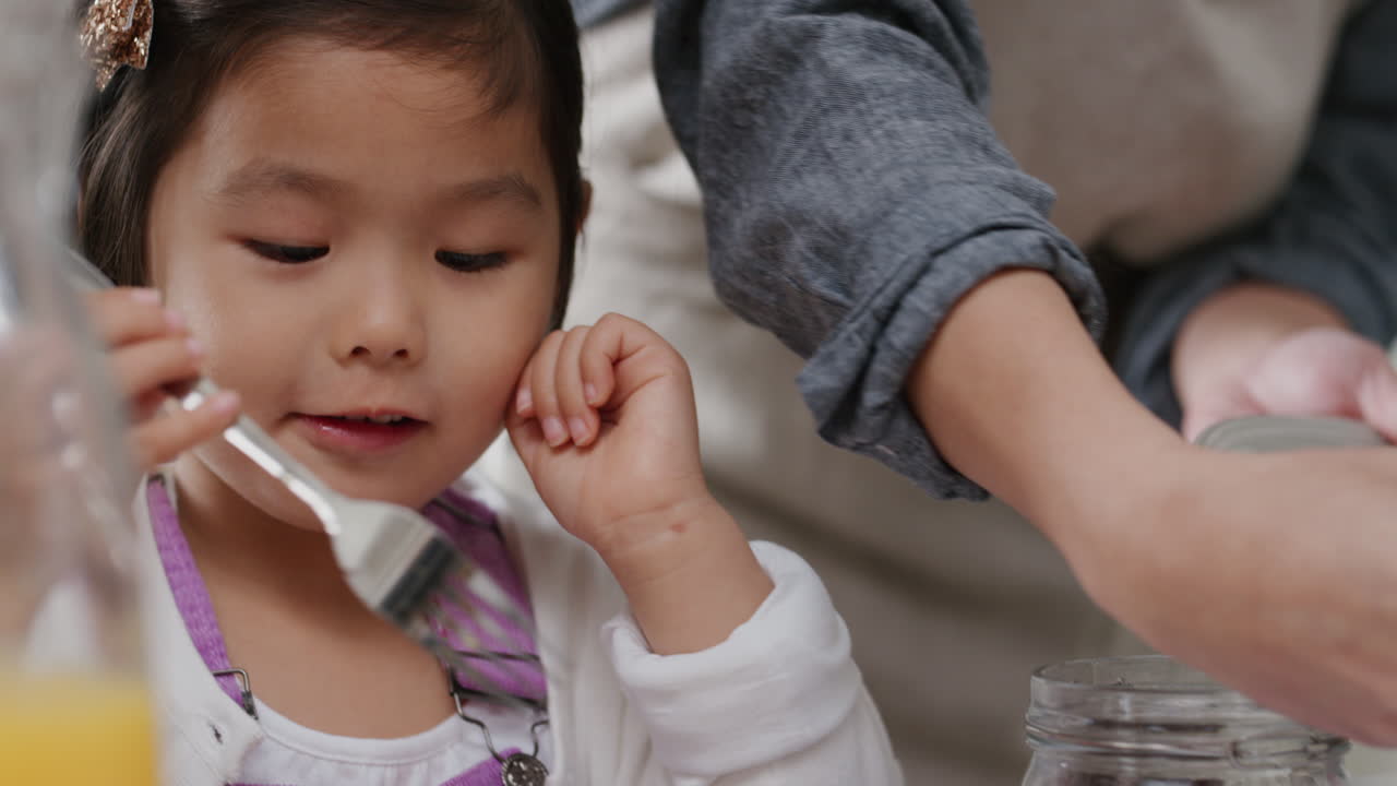 행복한 작은 아시아 소녀가 아침 식사로 신선한 와플을 먹고 집에서 부 ⁇ 에서 가족과 함께 맛있는 집에서 만든 식사를 즐기고 있습니다.