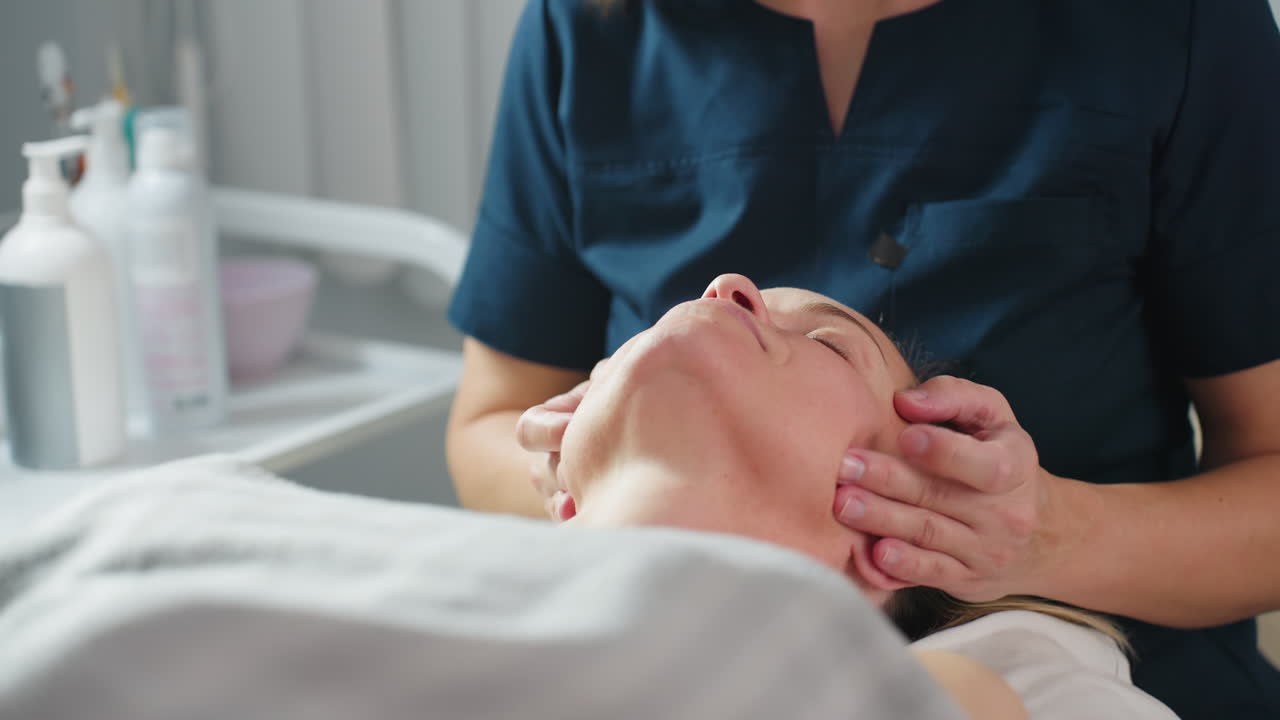 Bodywork therapist rubbing head and neck of visitor in spa with white background during relaxing facial and neck massage therapy session showcasing skilled hands and serene environment
