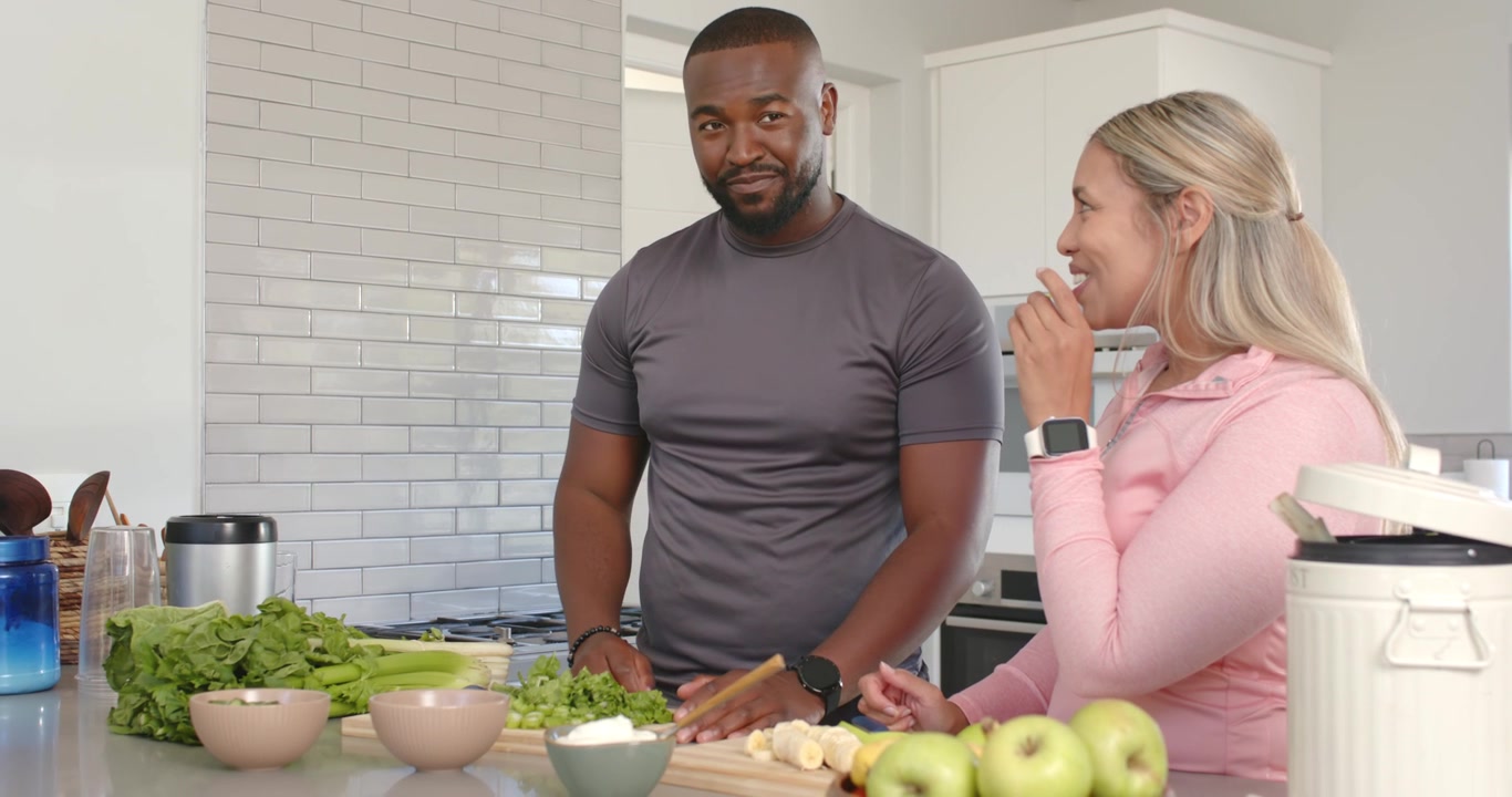 Casal afro-americano em casa provando, enquanto o homem pega um pedaço para verificar o sabor e corta a salada com uma faca.