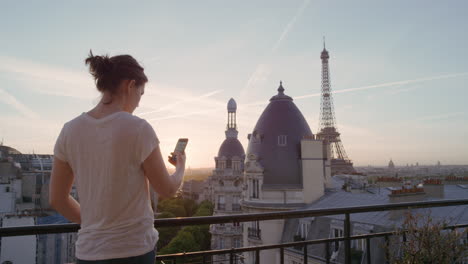 mujer feliz usando un teléfono inteligente tomando fotos disfrutando de compartir la experiencia de las vacaciones de verano en parís fotografiando la hermosa vista del atardecer de la torre eiffel en el balcón