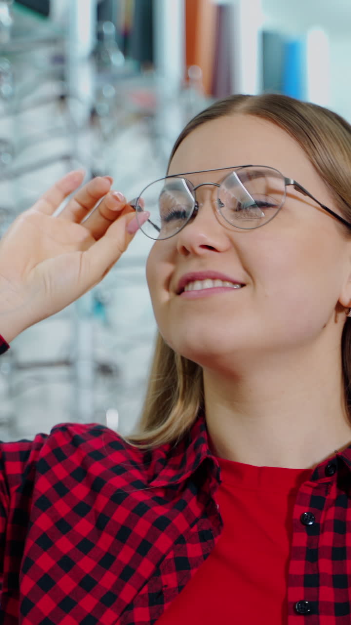 Smiling woman wearing new stylish glasses. Beautiful girl buying eyeglasses in the optical store. Female customer choosing spectacles. Vertical video