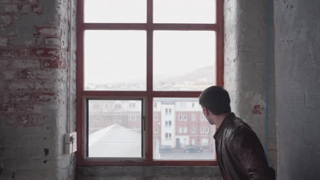 Männliches-Model-In-Lederjacke,-Das-Im-Studio-Aus-Dem-Fenster-Schaut