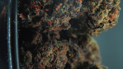 una toma cinematográfica macro vertical de una planta de cannabis, variedades híbridas de naranja, indica y sativa, flor de marihuana, en un soporte giratorio de 360 grados, grito brillante negro, cámara lenta, video 4k, iluminación de estudio