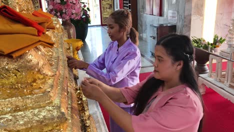 women applying gold leaf at a thai temple