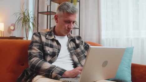 hombre trabajando en una computadora portátil con expresión pensativa reflexionando sobre una respuesta de solución en la habitación de casa