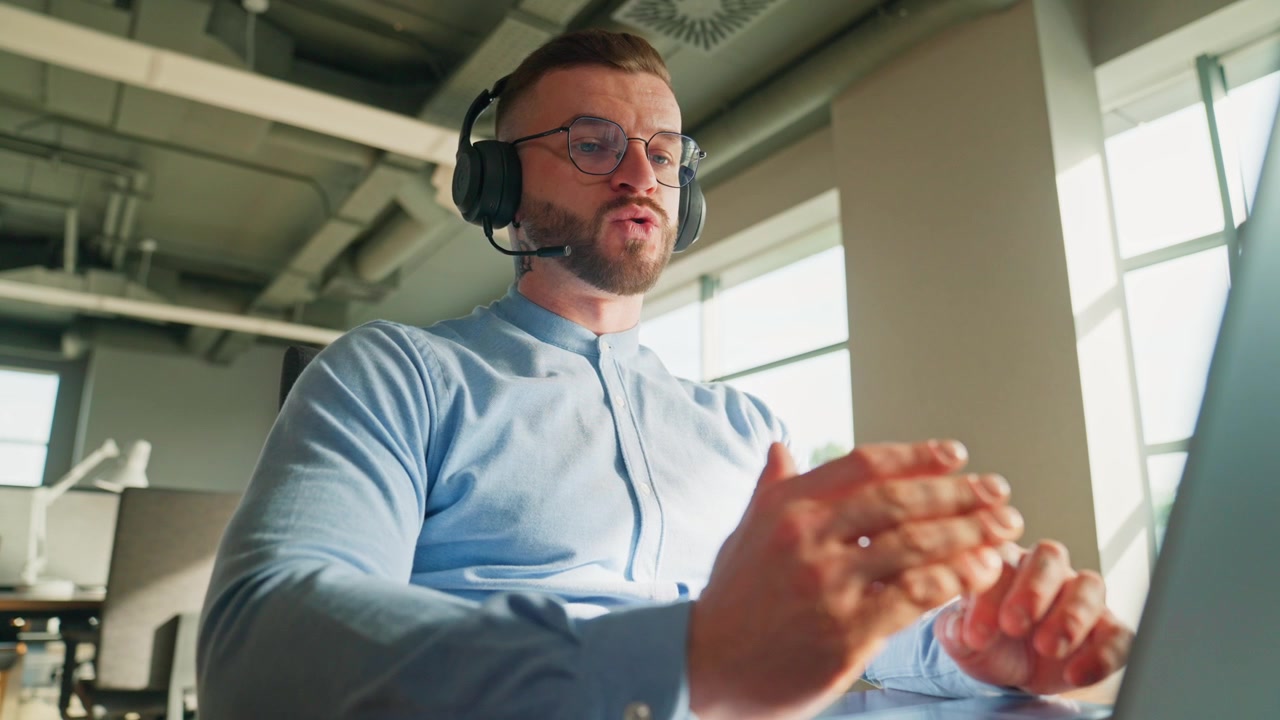 Professionista con cuffie che parla in videochiamata in un ufficio moderno