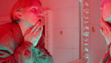 man washing face and looking in mirror in bathroom with red light