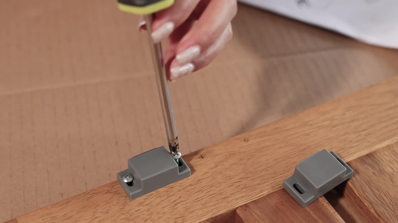 Close-up of hands using a screwdriver to assemble furniture on a wooden surface in a well-lit environment