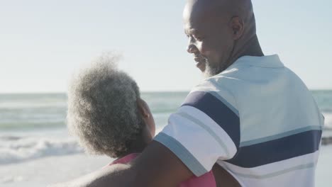 happy senior african american couple embracing at beach, in slow motion