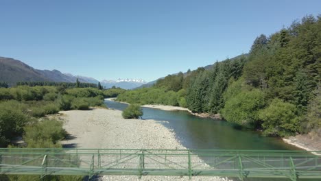 Dolly-Aéreo-En-Río-Y-Puente-Elevado-Rodeado-De-Pinos-Y-Montañas,-Pasarela-Rio-Azul,-Patagonia-Argentina