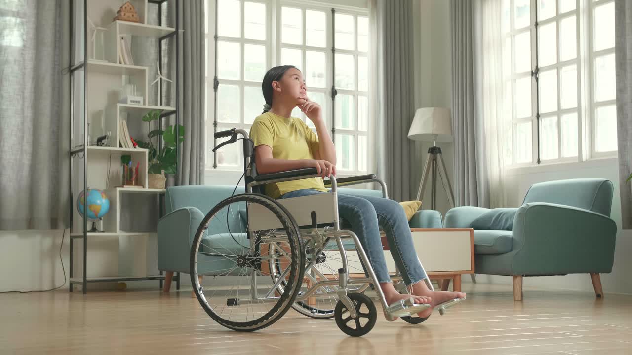 Asian Kid Girl Sitting In A Wheelchair And Thinking About Something Then Raising Her Index Finger And Eyes Wide Open In Living Room