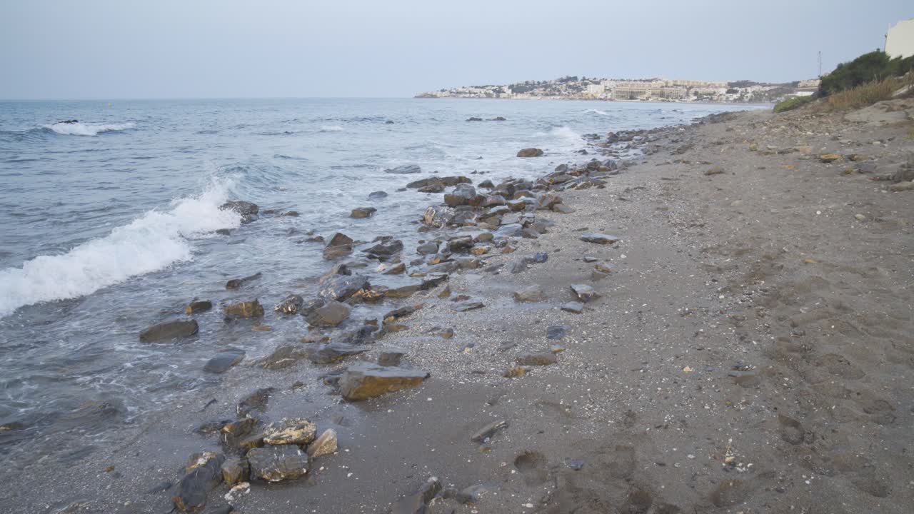 Light surf gently washes in as the cool morning light shines on the rocky beach looking toward Cala de Mijas on the Costa Del Sol in Southern Spain