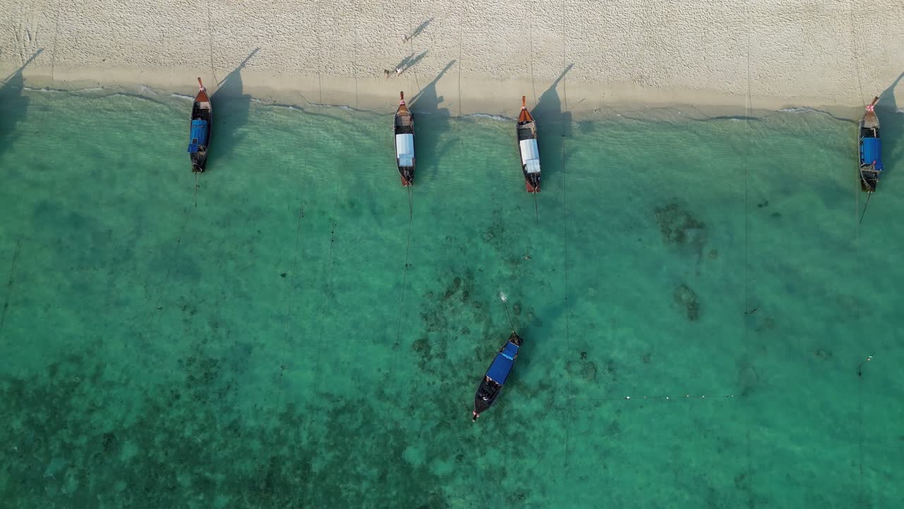Traditional longtail boats line the shore of Long Beach, Koh Phi Phi, with crystal-clear turquoise waters below.