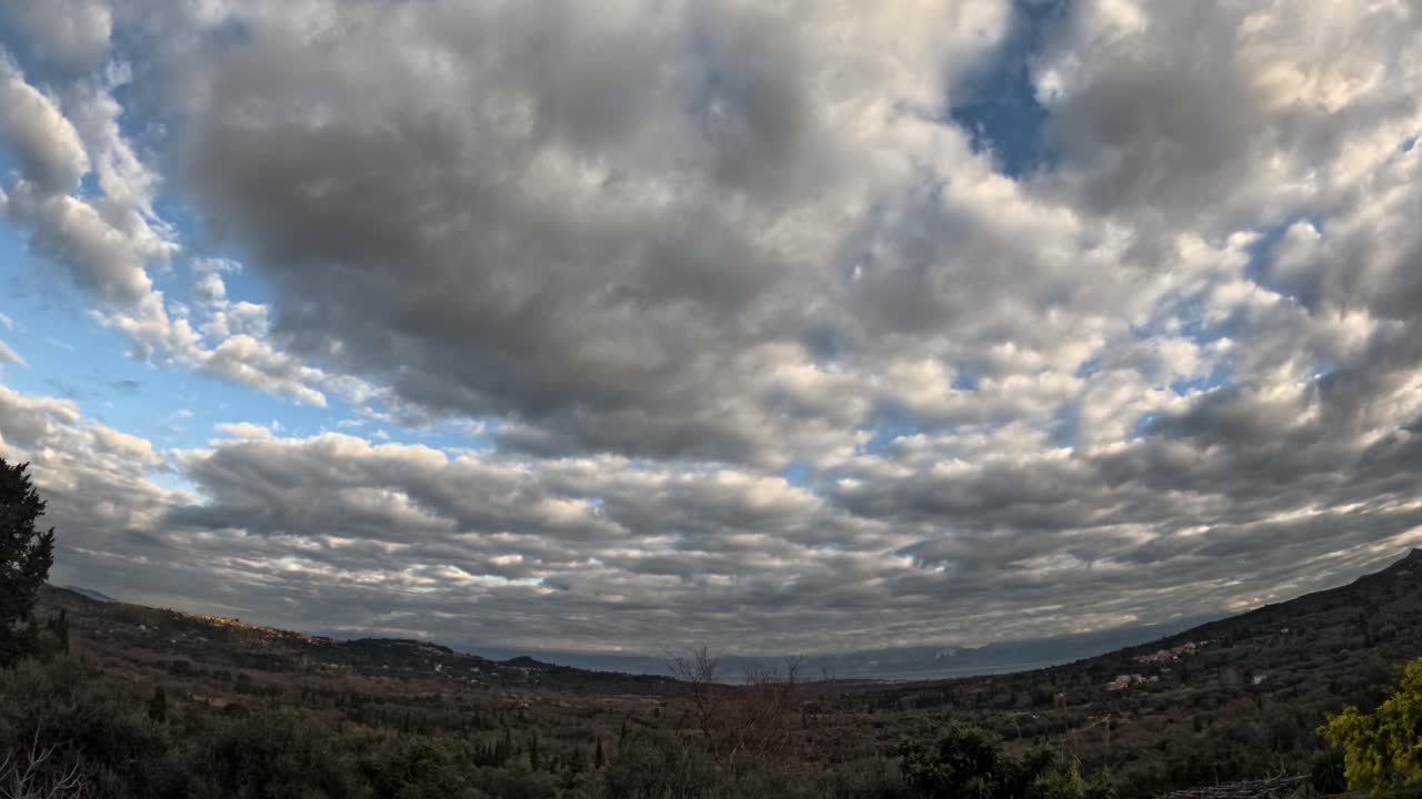Dramatisk timelapse af hurtigt bevægende, bløde, hvide cumulusskyer, der ruller hen over en klar, blå himmel over grønne landlige bakker og dale på Korfu i Grækenland, og fanger naturens og vejrets dynamiske skønhed