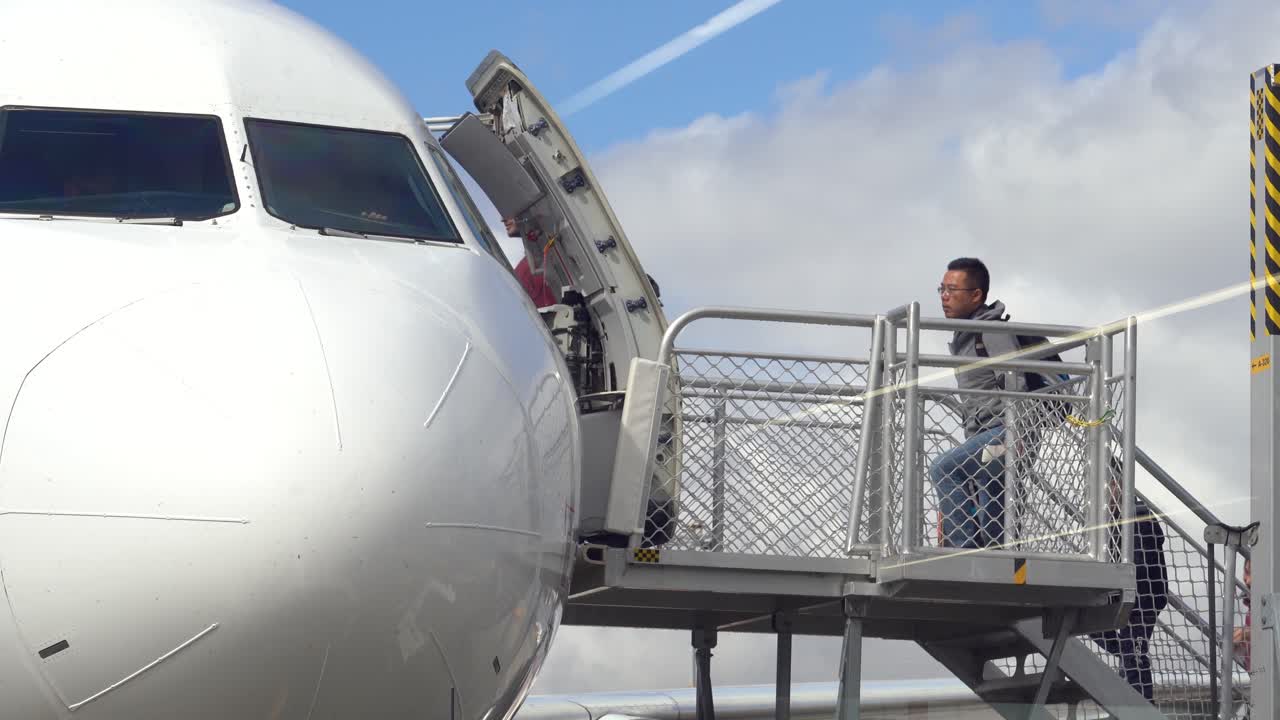 Footage of airport passengers boarding into the commercial aircraft airplane by climbing the movable stairs.