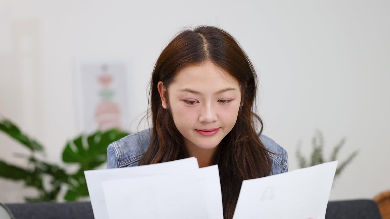 明るいホームオフィスのソファで書類を確認する、自然光が差し込む若い女性