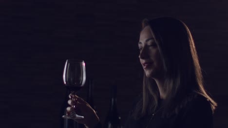 mujer morena levantando una copa de vino tinto en un estudio romántico de ambiente oscuro, mirando directamente a la cámara