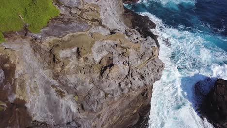 beautiful crashing blue waves at spitting cave in honolulu hawaii with jagged cliffs and vibrant greenery - aerial top down dolly