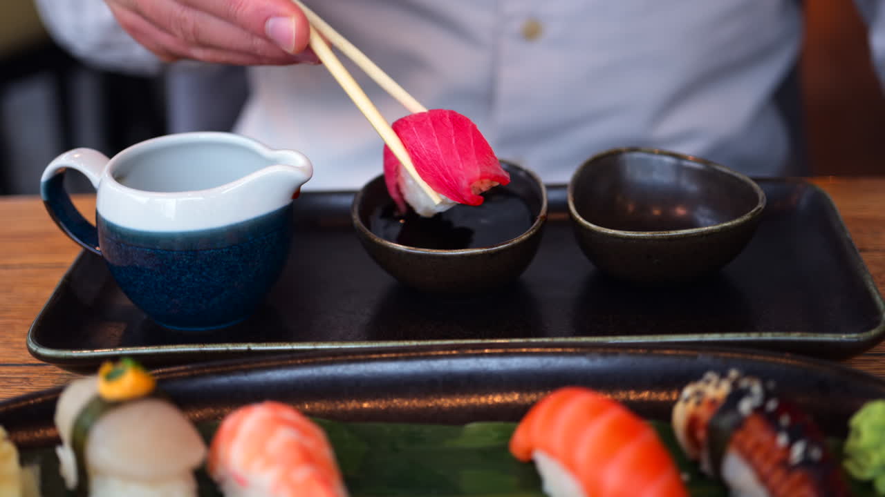 Close up of a man eating multiple nigiri from a black tray at a restaurant