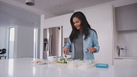 mujer en la cocina preparando comida alta en proteínas y poniendo porciones en contenedores de plástico