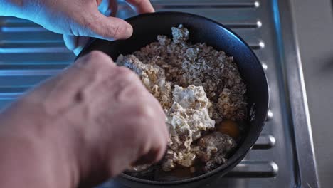 Hands-Mixing-Oatmeal,-Cheese,-Eggs,-And-Water-In-A-Bowl
