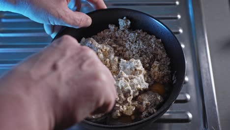 hands mixing oatmeal, cheese, eggs, and water in a bowl