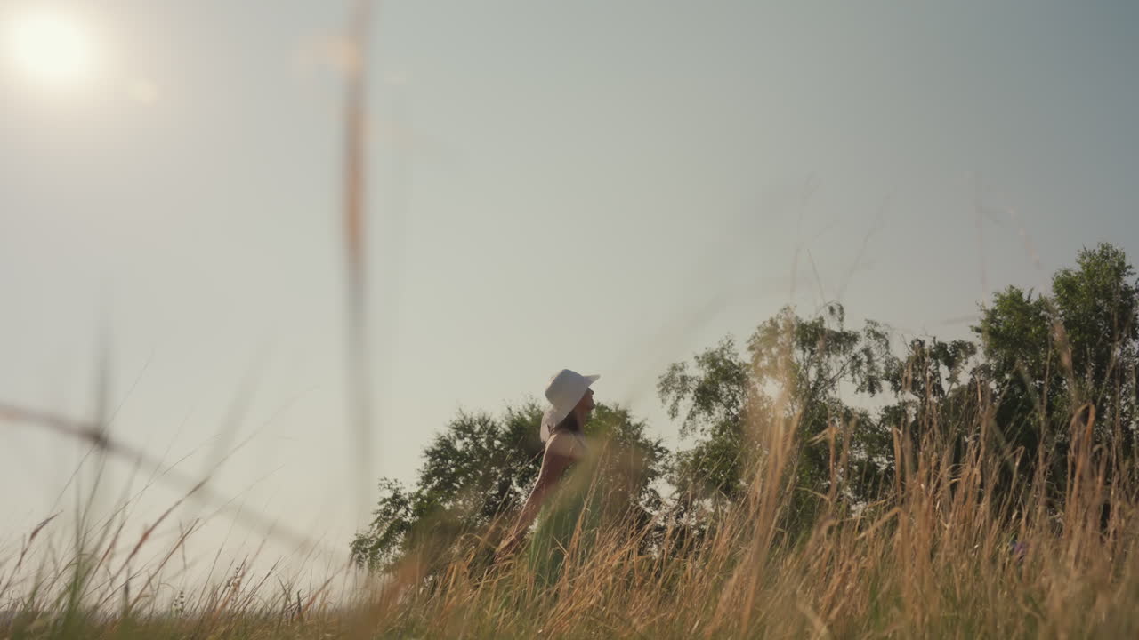 woman in green dress dancing with raised arms in golden grassy field during sunlit afternoon while photographer films from low angle capturing warm glow