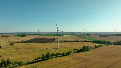 Aerial-view-of-wind-turbines-scattered-across-golden-farmland,-highlighting-the-blend-of-agriculture-and-renewable-energy-on-a-clear-day