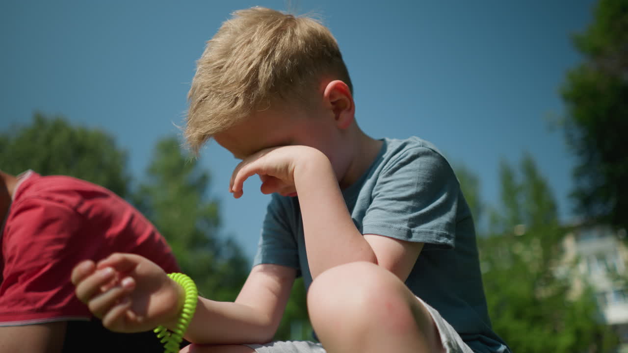 파란 셔츠를 입은 피곤해 보이는 작은 소년은 왼손으로 얼굴을 문지르며, 오른손에는 레몬색 인 고무가 있고, 몇몇은 근처에 무을 고 있다.