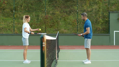 vista lateral de una pareja feliz jugando tenis en la cancha al aire libre en un día de verano