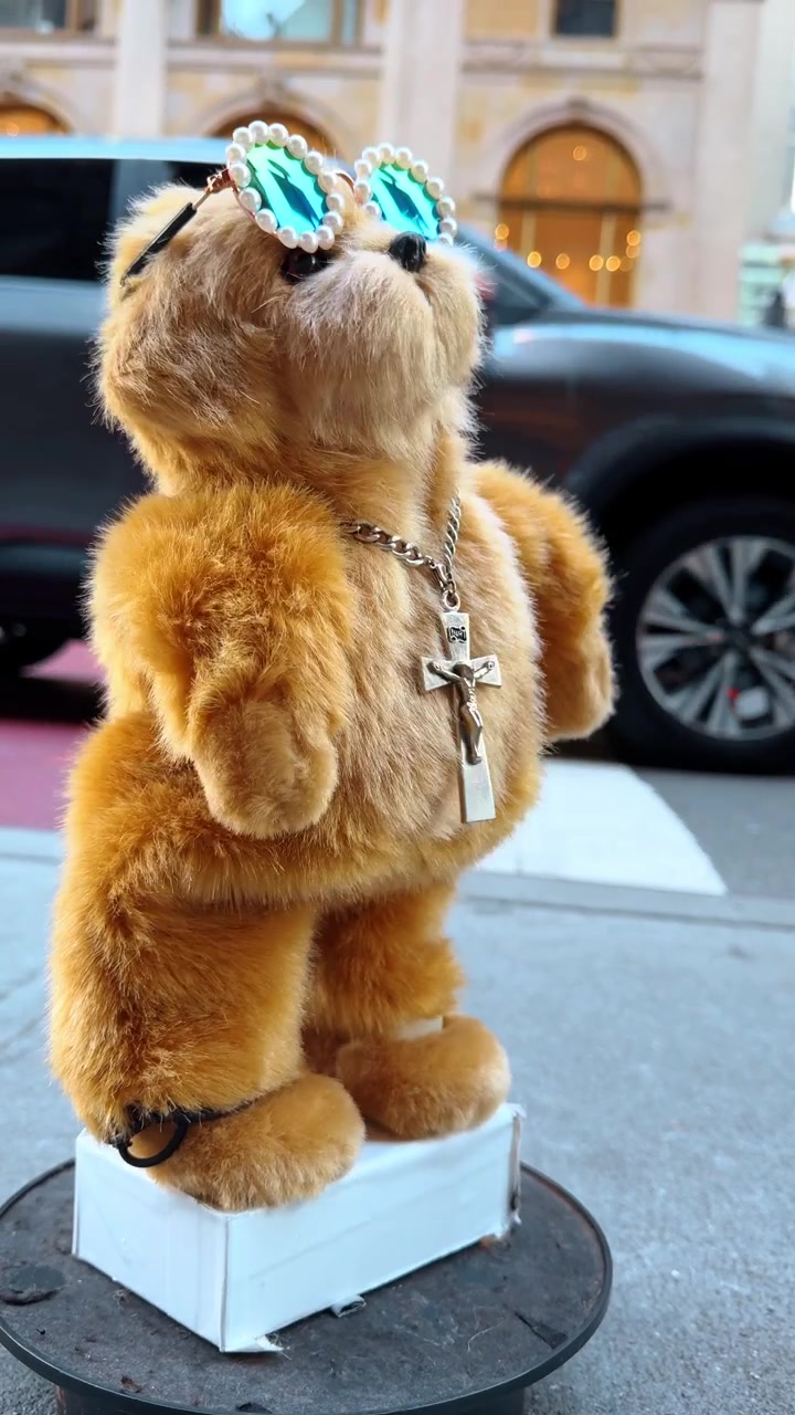 New York, USA, 5 ottobre 2025: Vista posteriore di un cane di peluche su un marciapiede cittadino. Vista da dietro di un giocattolo di peluche meccanico marrone in piedi su una base bianca in un ambiente urbano.
