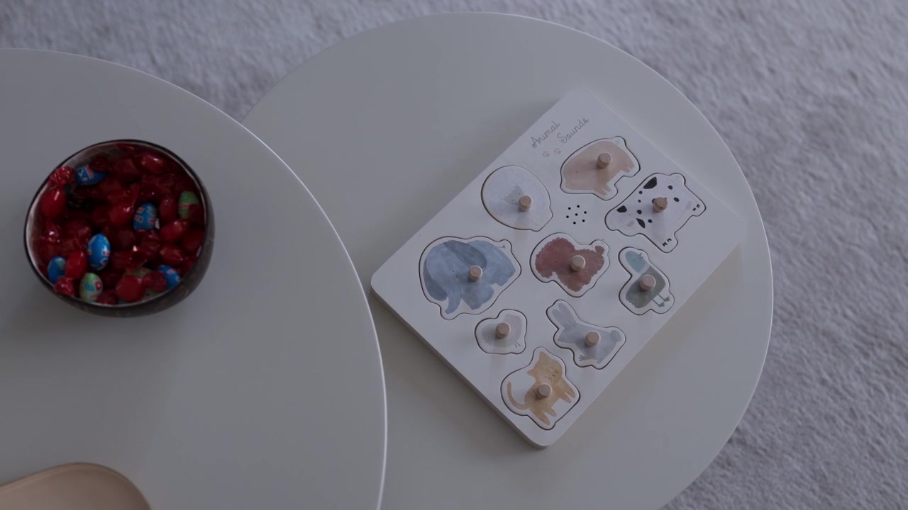 Puzzle di animali in legno con pioli accanto a una ciotola di vetro di caramelle rosse su un tavolo rotondo bianco