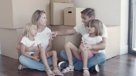 family couple and two girls sitting on floor near boxes