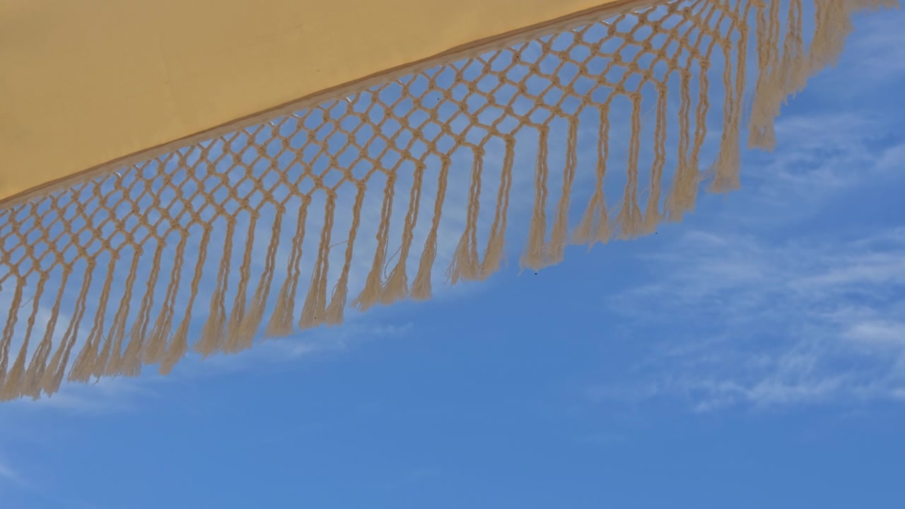 Beautiful 4K low-angle shot of white fringed macrame umbrellas at a luxury beach resort. Features an organized row of sunbeds, tropical palm trees, and a clear blue sky.