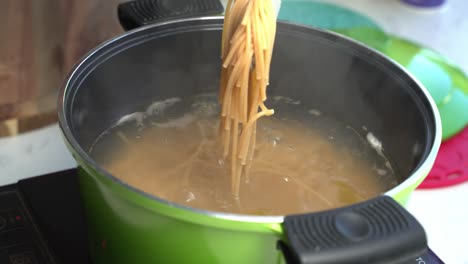 close up view of boiling pasta in green pot with steam, lifting spaghetti with kitchen tongs, static
