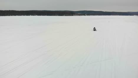 aerial shot of a man driving his snowmobile towards the camera on indalsalven in timra, sundsvall, sweden-1