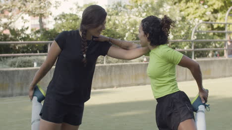 futbolistas femeninas estirando las piernas dobladas en la rodilla, abrazándose unos a otros hombro