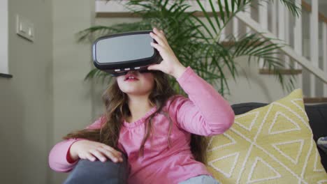 caucasian girl wearing vr headset, sitting on sofa and having fun