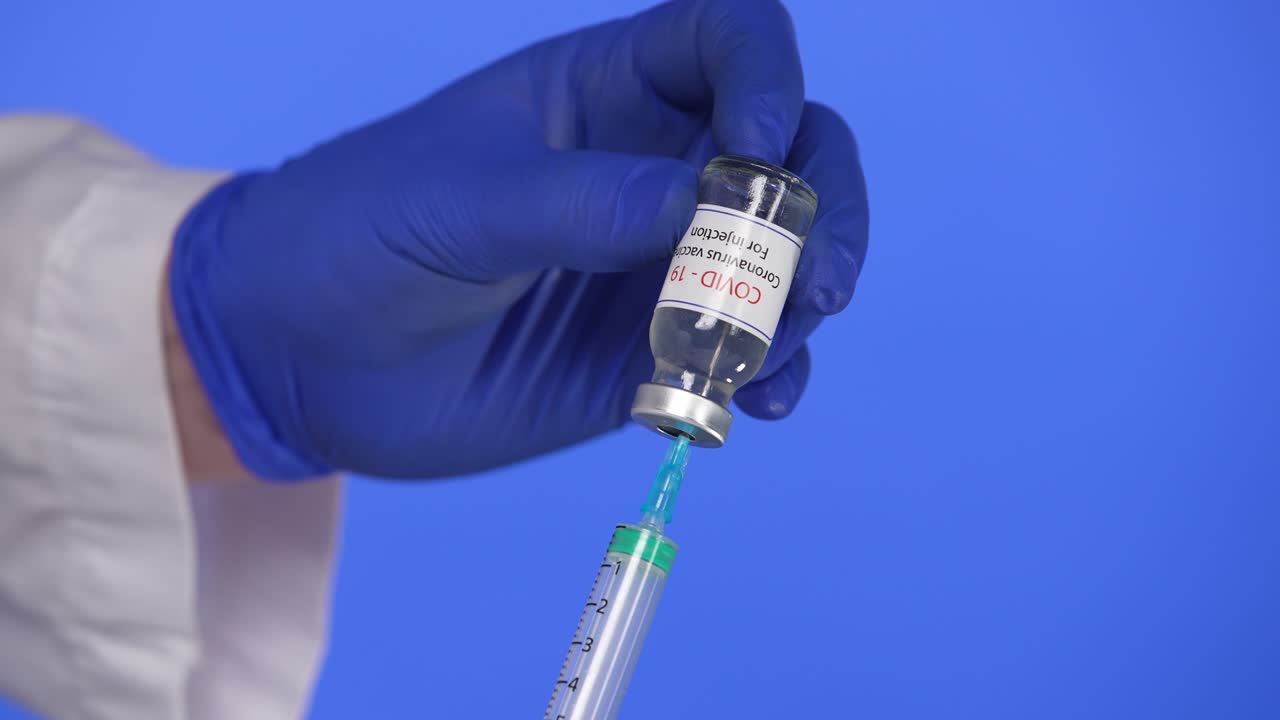 un médico con guantes quirúrgicos azules marca una vacuna contra el coronavirus en una jeringa para vacunar contra una epidemia mundial de sars-cov-2. pantalla azul, clave de croma. primer plano. cámara lenta